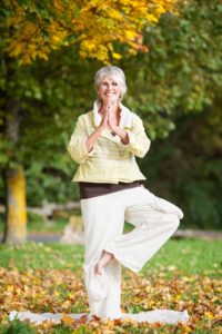 21246783 - full length of smiling senior woman with arms outstretched standing on one leg while doing yoga in park