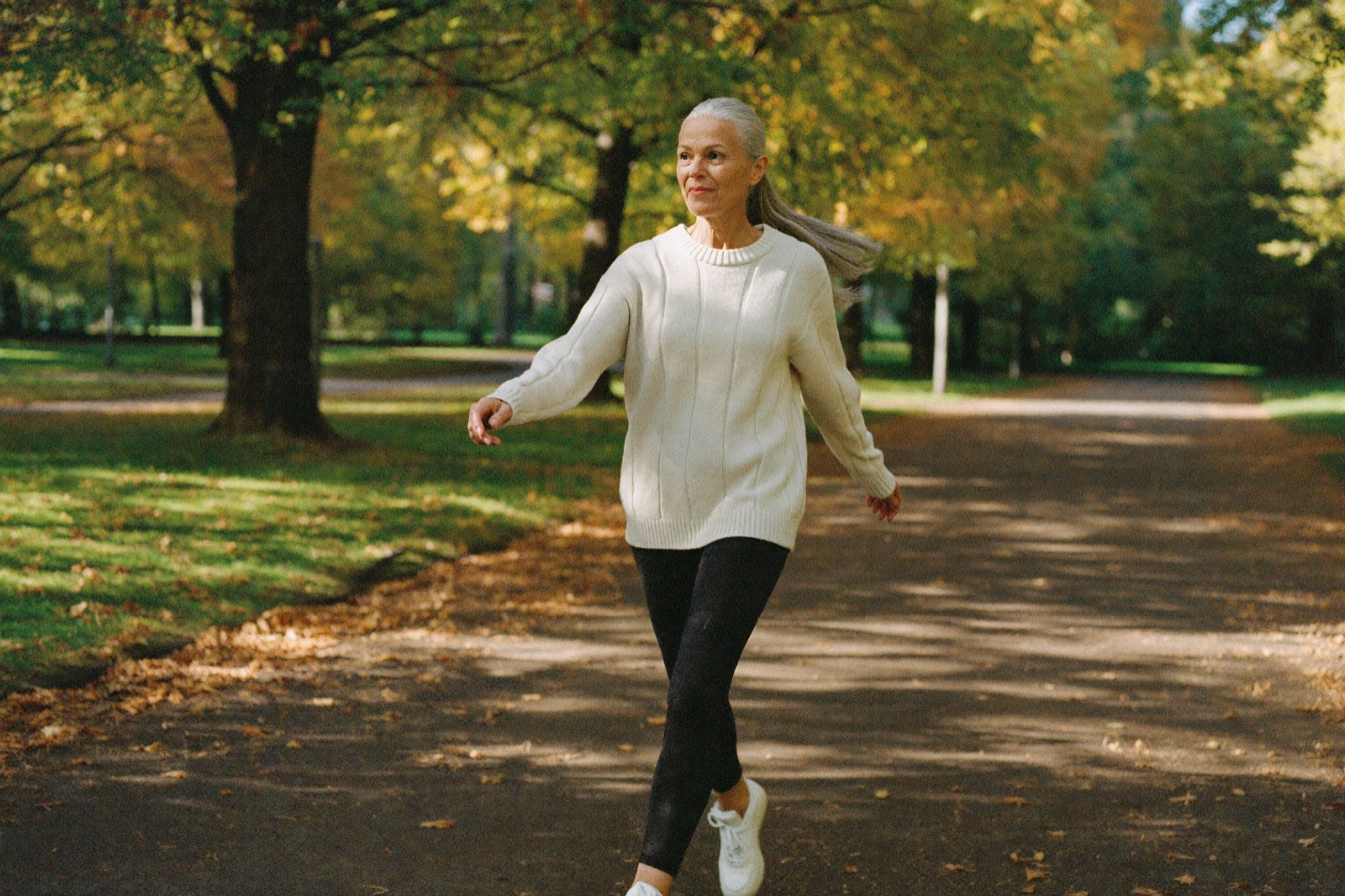 Mature woman walking confidently on autumn tree-lined path
